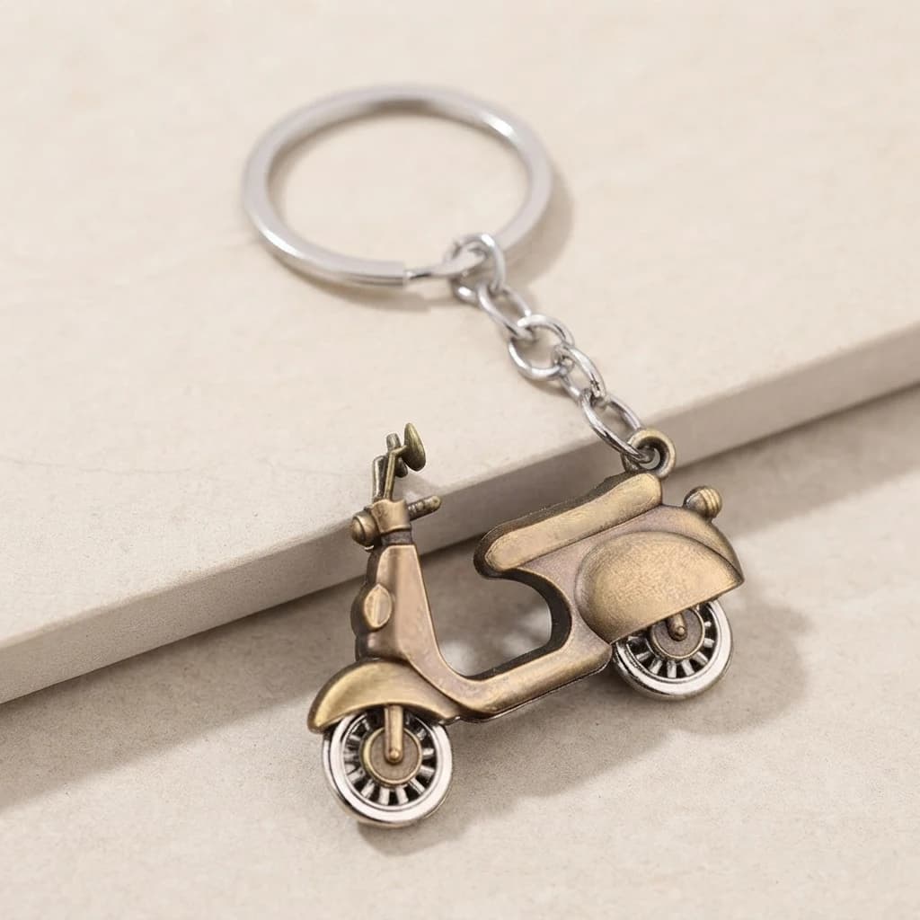 Three-quarter view of a vintage-style scooter keyring displaying its contoured body and silver wheels.