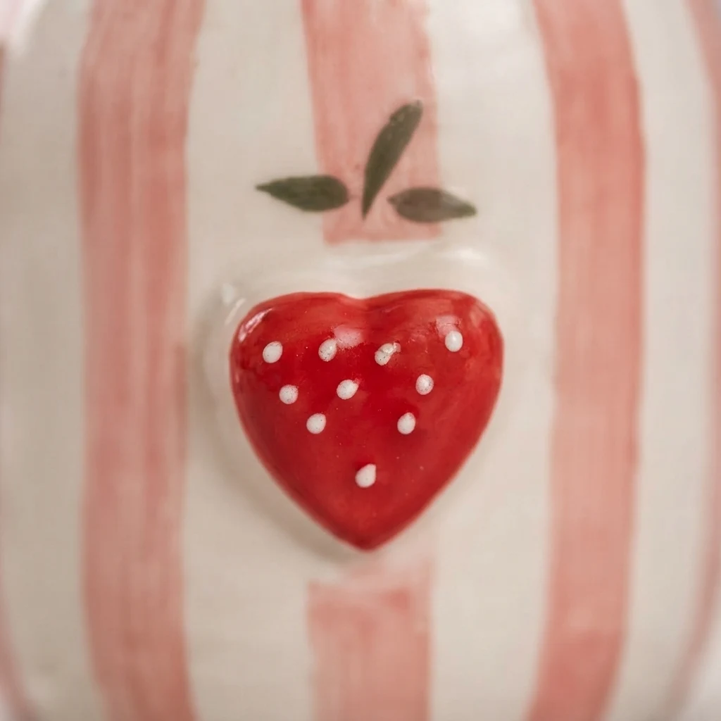 Close view of the raised red strawberry motif and soft pink stripes on the mug.